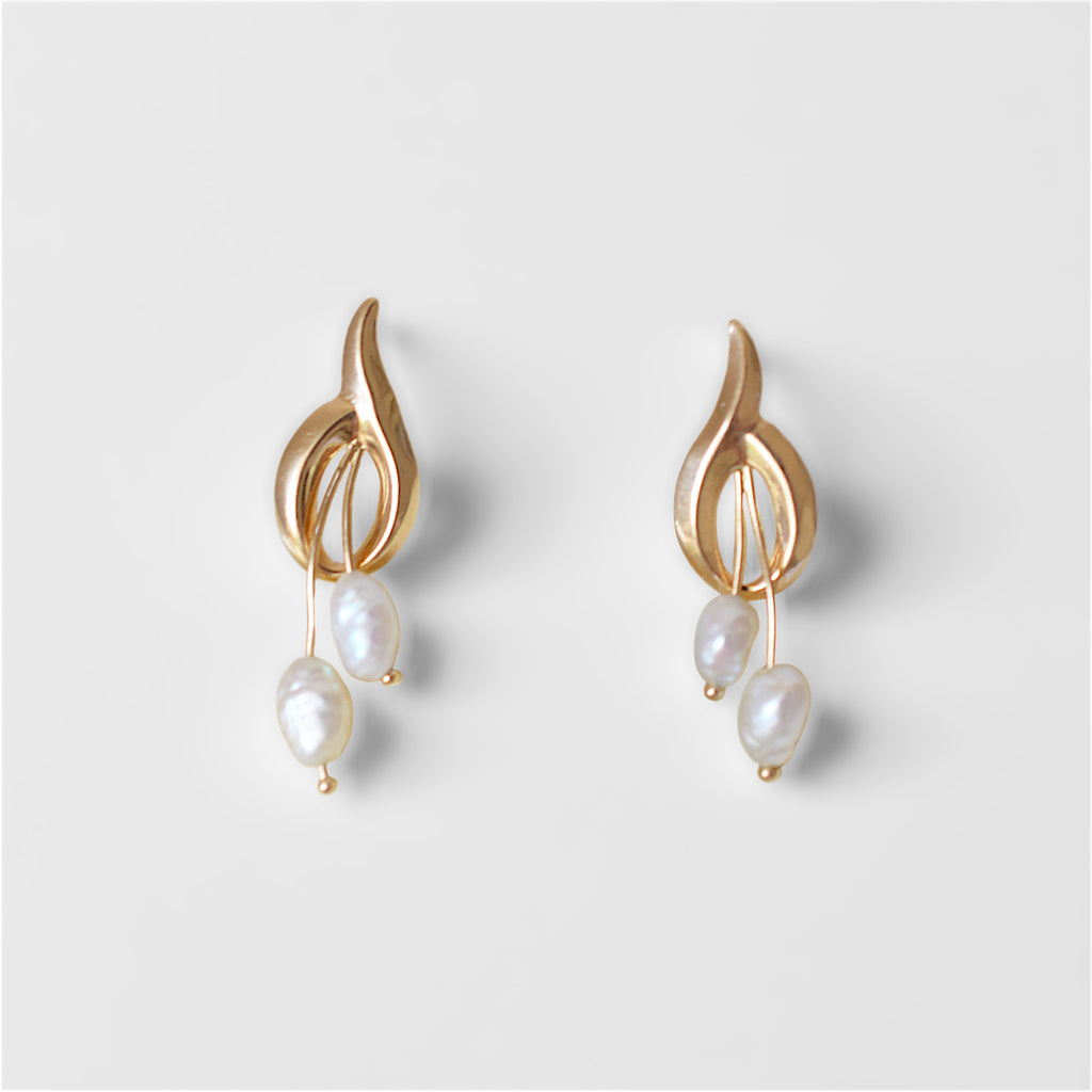 A pair of elegant 14K gold earrings, each featuring a polished, abstract gold top piece with openwork details. From each gold design, two irregularly shaped white baroque pearls dangle at varying lengths. The earrings are displayed side-by-side on off-white surface.