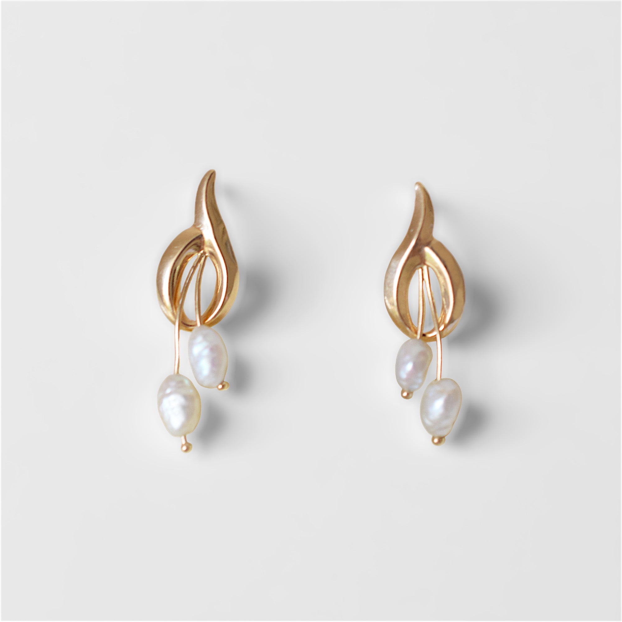 A pair of elegant 14K gold earrings, each featuring a polished, abstract gold top piece with openwork details. From each gold design, two irregularly shaped white baroque pearls dangle at varying lengths. The earrings are displayed side-by-side on off-white surface.