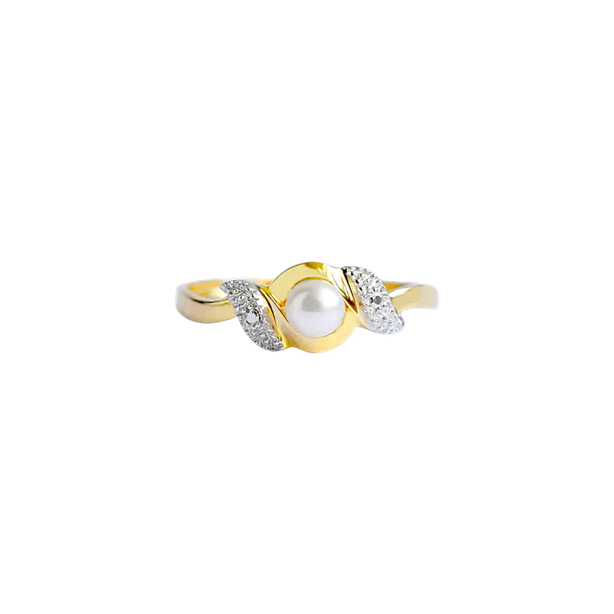 An elegant 18k gold bypass ring featuring a luminous central pearl, with sparkling textured details on each side.