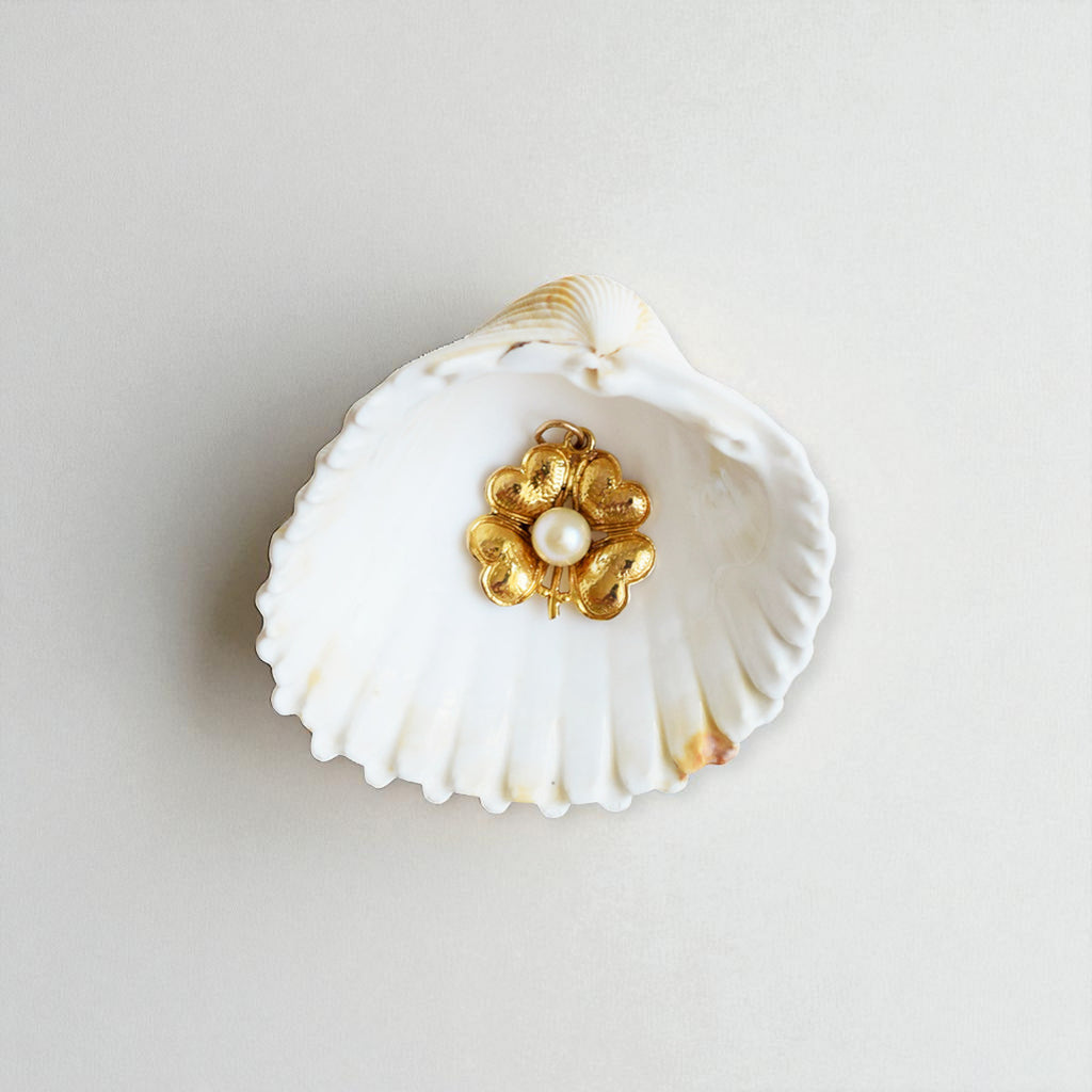 Gold flower-shaped earring with pearl center on a white shell against a light gray background