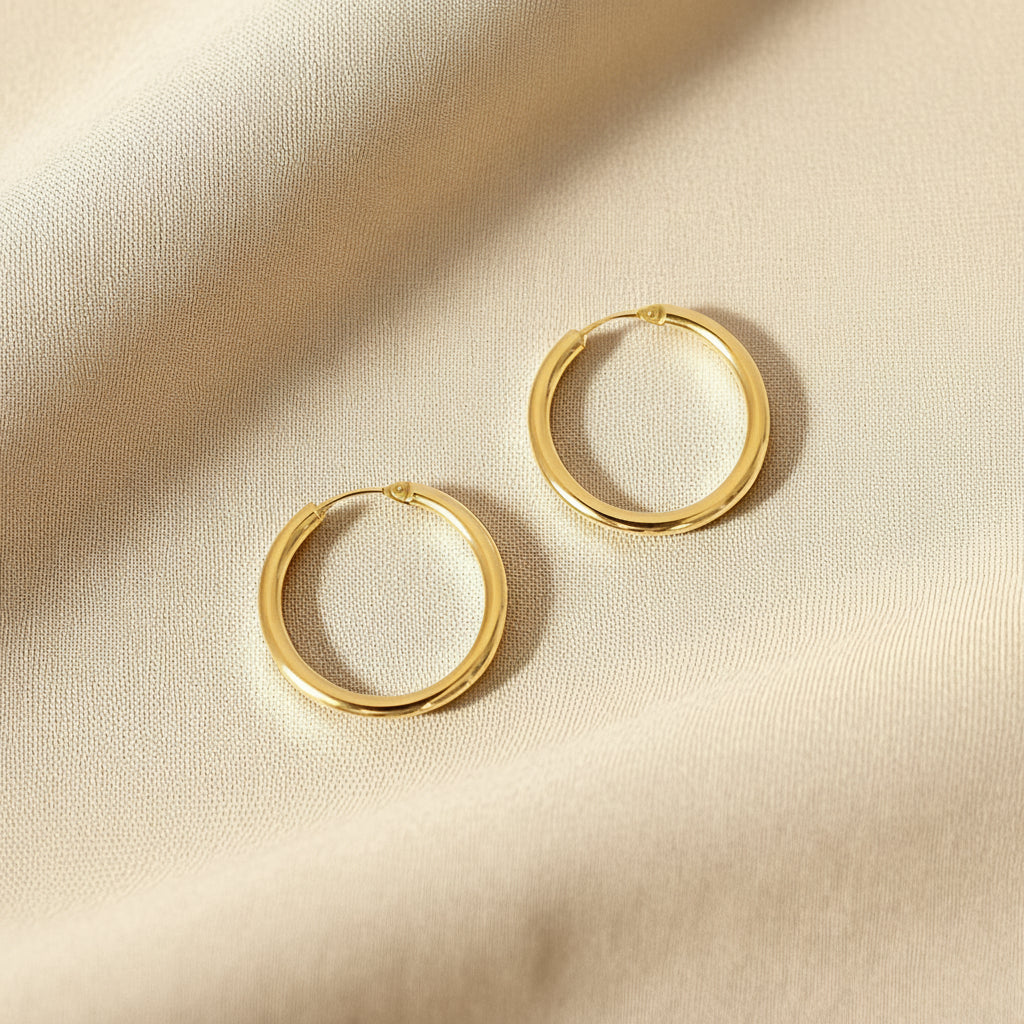 Classic 18 Karat Yellow Gold Hoop Earrings with a smooth, polished finish against a lightbrown fabric.