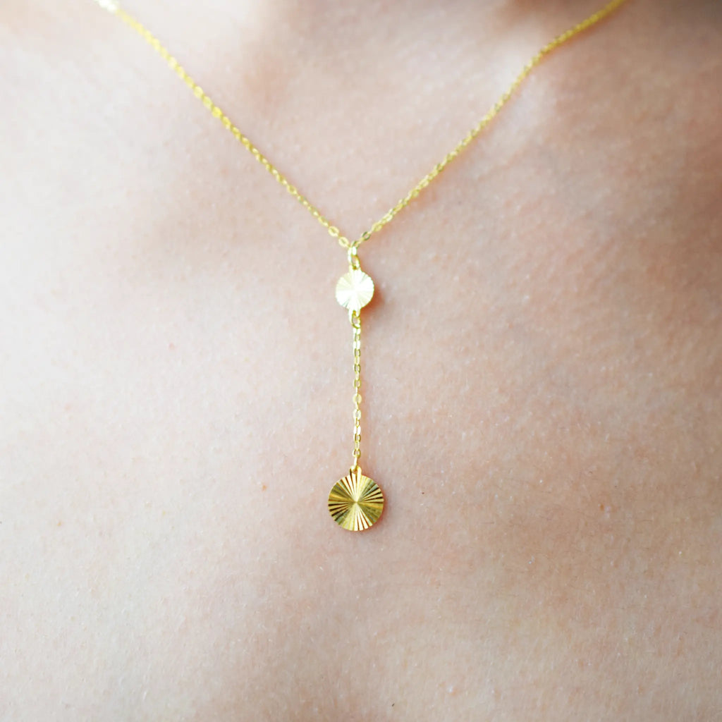 Gold necklace with a sunflower pendant on a person's neck against a neutral background