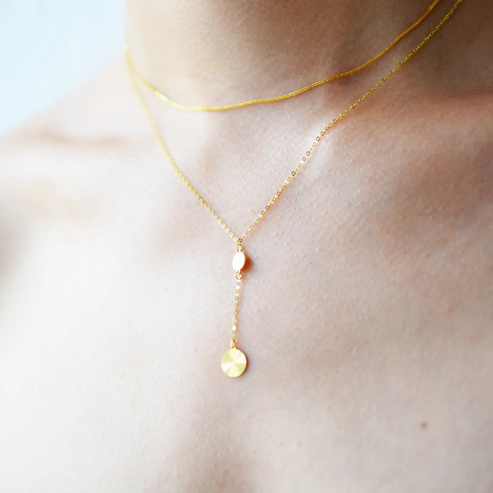 Gold necklace with a pendant on a person's neck against a light background