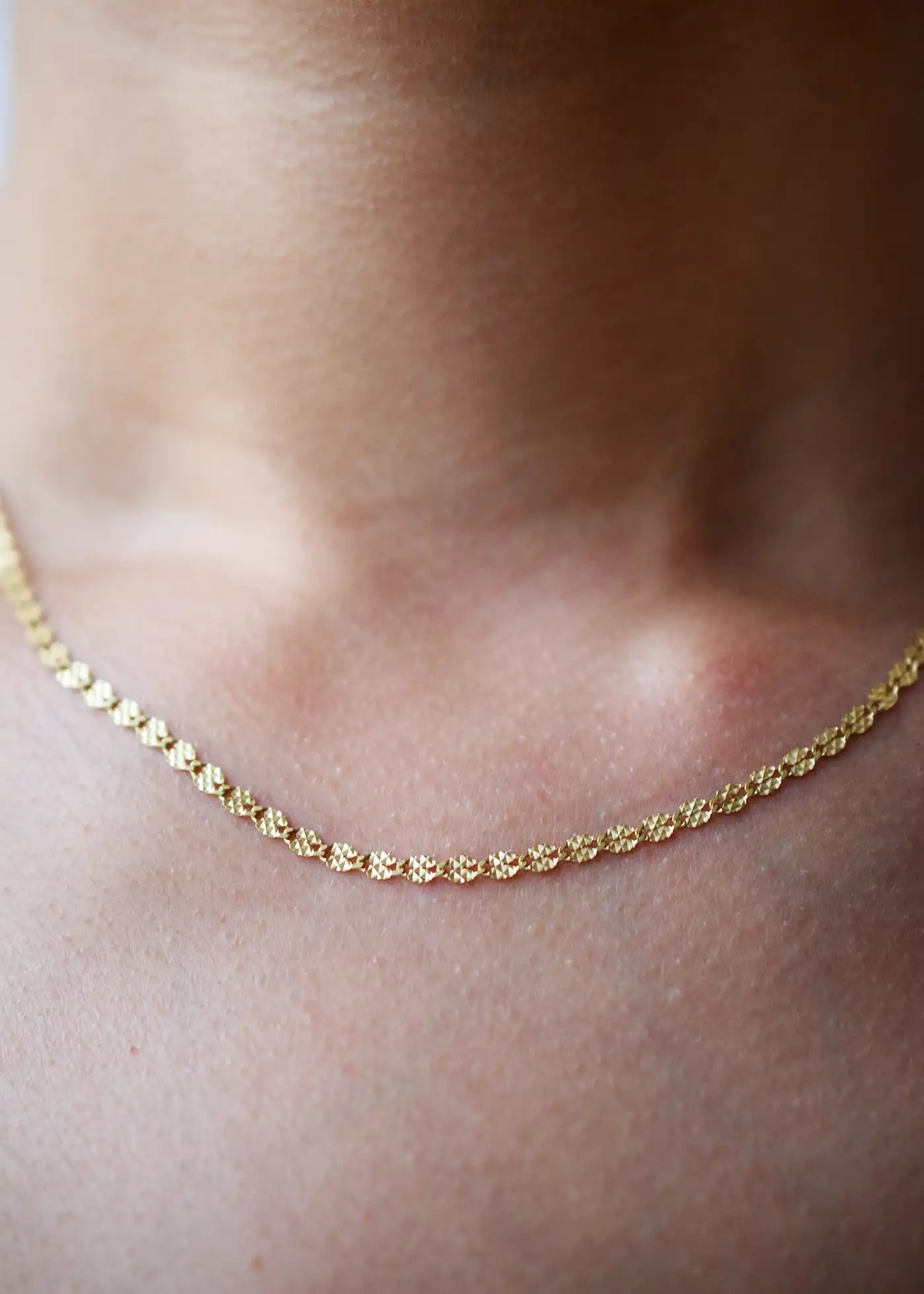 Delicate 14 Karat Yellow Gold chain necklace featuring shimmering diamond-cut flat oval links, worn gracefully on a model's neck.