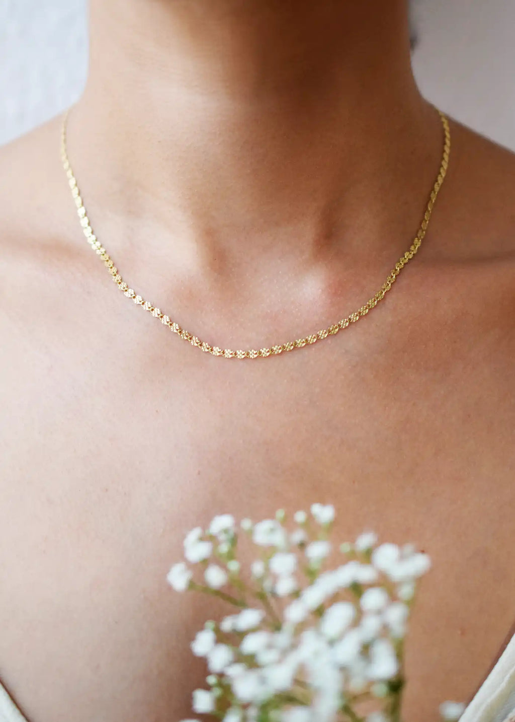 Delicate 14 Karat Yellow Gold chain necklace featuring shimmering diamond-cut flat oval links, worn gracefully on a model's neck.