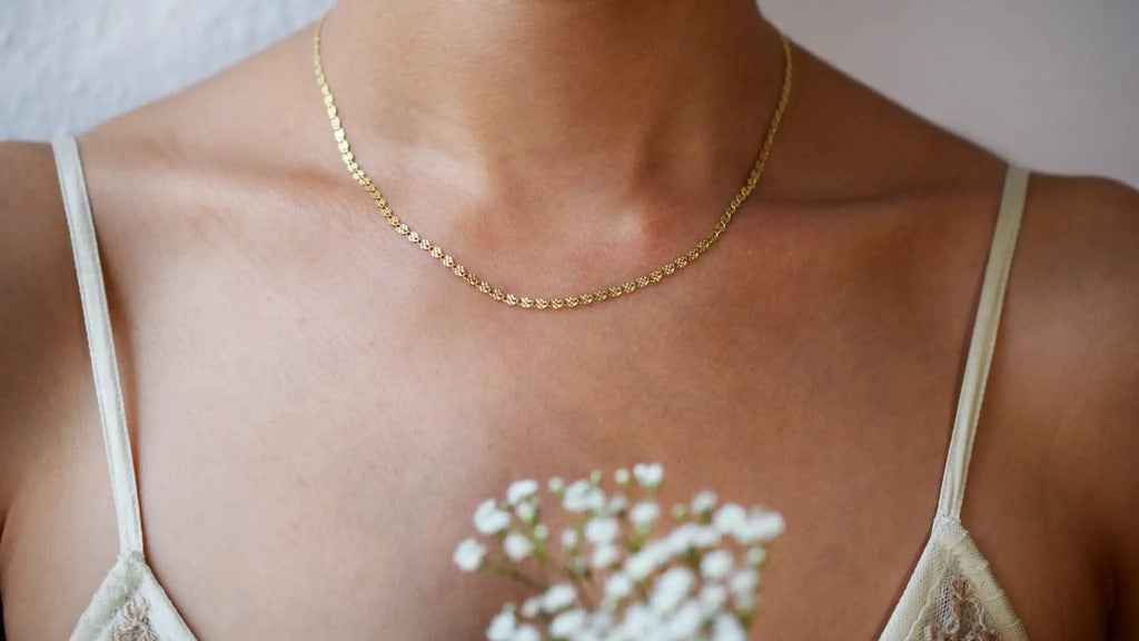 Delicate 14 Karat Yellow Gold chain necklace featuring shimmering diamond-cut flat oval links, worn gracefully on a model's neck.
