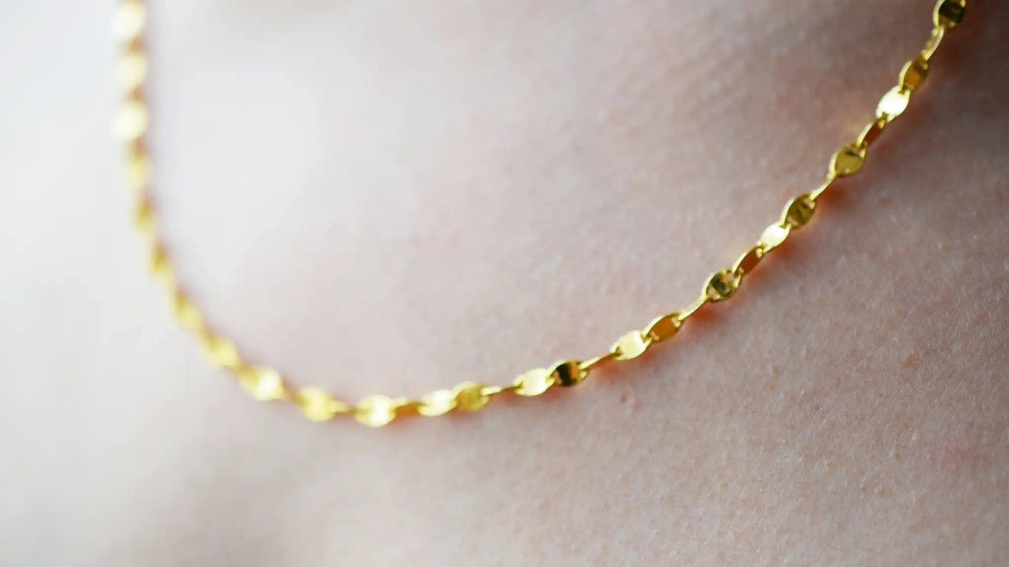 Delicate 21 Karat Yellow Gold necklace featuring a shimmering flat link chain that creates a subtle twisted effect when worn, visible on a model's neck.