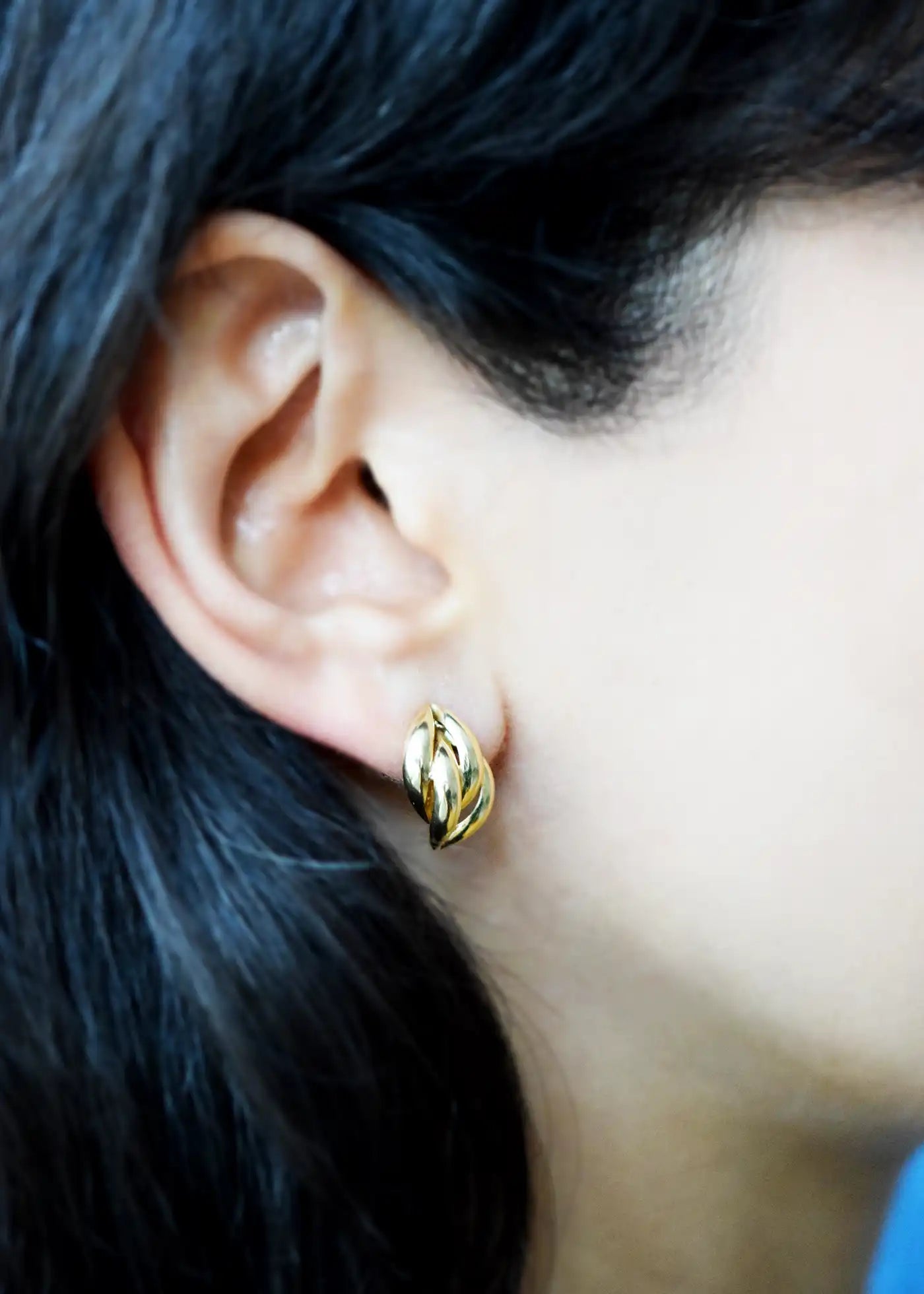 Elegant 14 Karat Yellow Gold post earrings with a highly polished, curved leaf-like design, worn on a model's ear.
