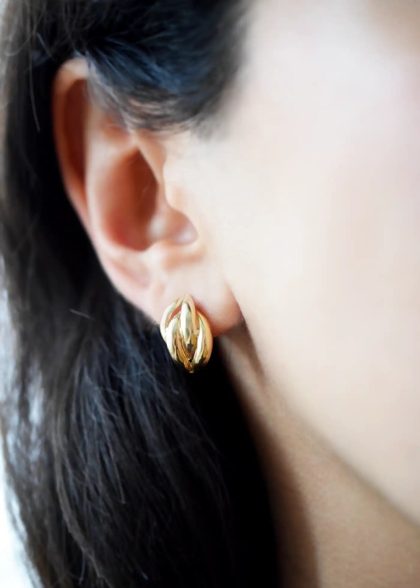 Elegant 14 Karat Yellow Gold post earrings with a highly polished, curved leaf-like design, worn on a model's ear.