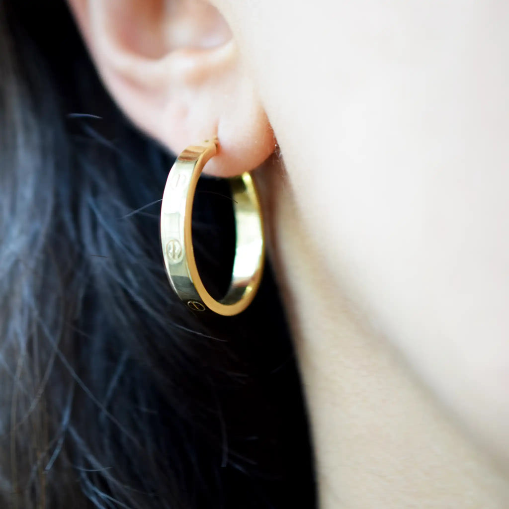Elegant 18 Karat Yellow Gold flat hoop earrings with prominent screw-head details, worn on a model's ear.