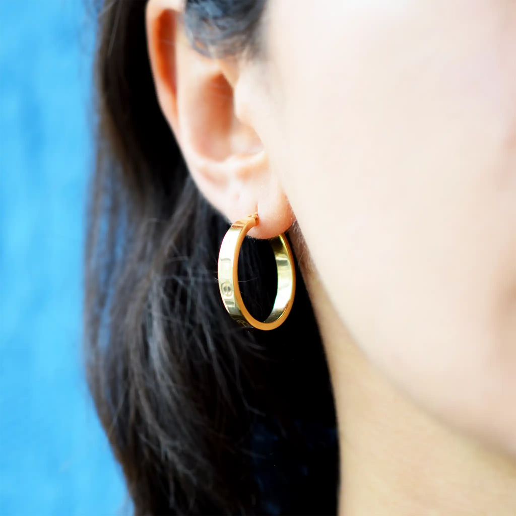 Elegant 18 Karat Yellow Gold flat hoop earrings with prominent screw-head details, worn on a model's ear.