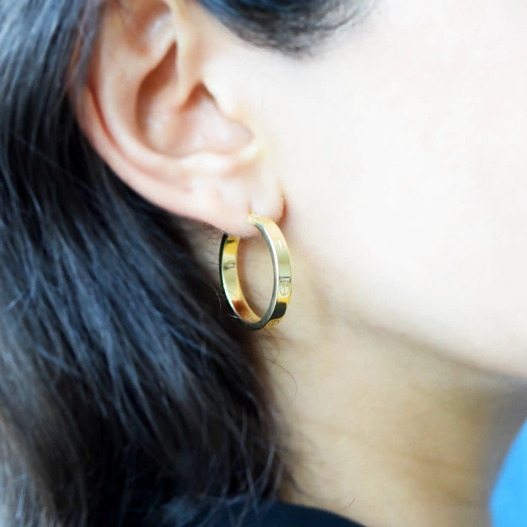 Elegant 18 Karat Yellow Gold flat hoop earrings with prominent screw-head details, worn on a model's ear.