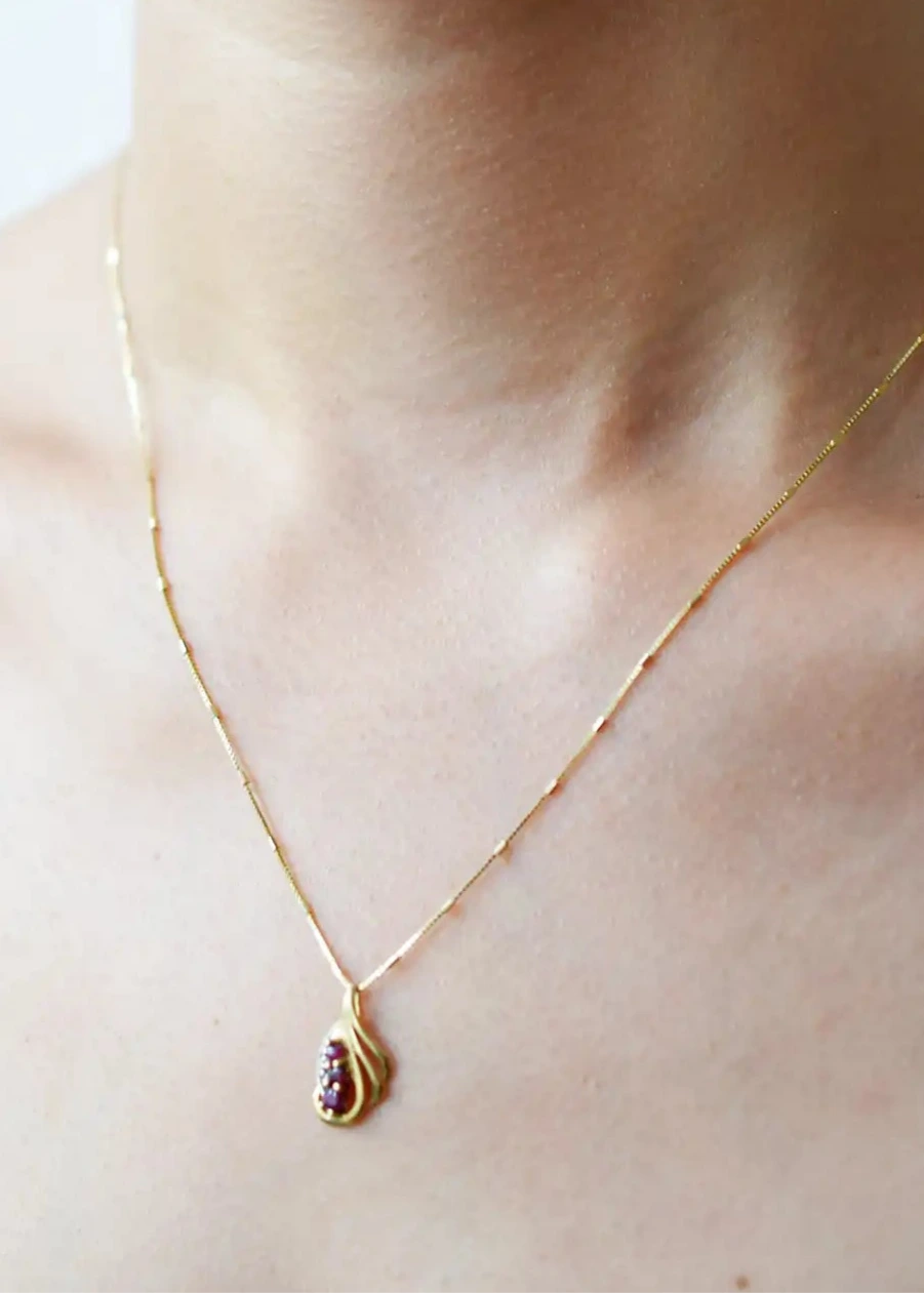 Elegant 18 Karat Yellow Gold vintage-style pendant with a sculpted, flowing design, featuring three vibrant rubies and a sparkling diamond accent.