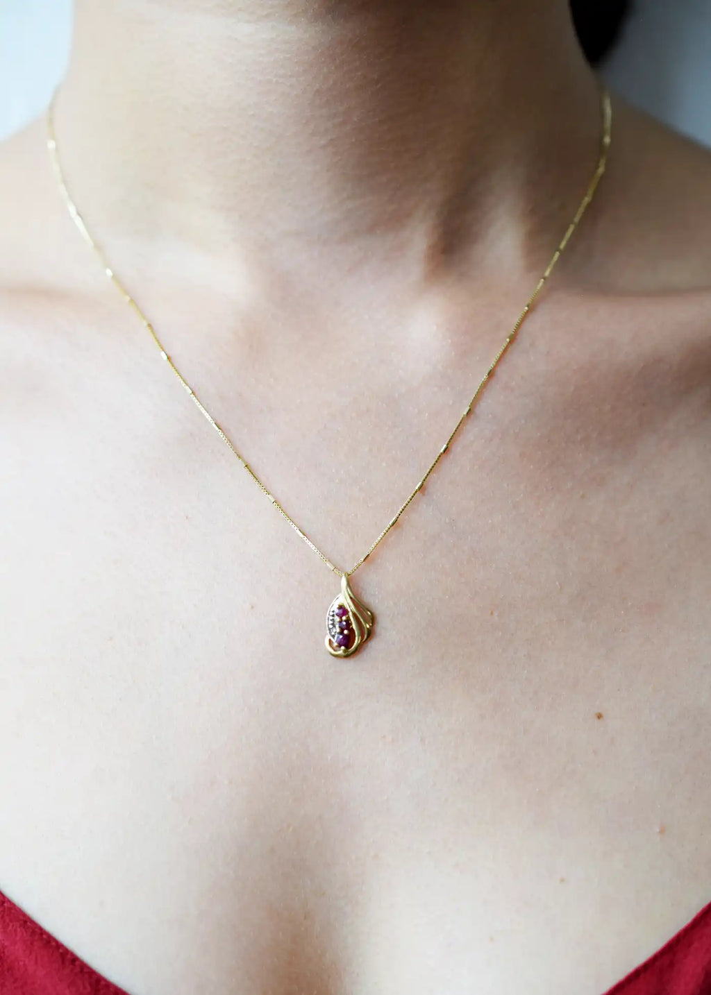 Elegant 18 Karat Yellow Gold vintage-style pendant with a sculpted, flowing design, featuring three vibrant rubies and a sparkling diamond accent.