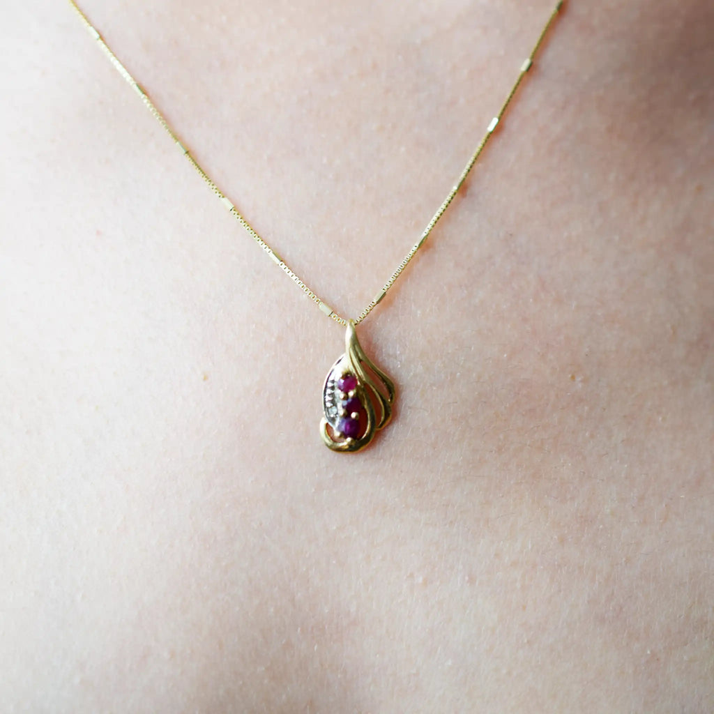 Elegant 18 Karat Yellow Gold vintage-style pendant with a sculpted, flowing design, featuring three vibrant rubies and a sparkling diamond accent.