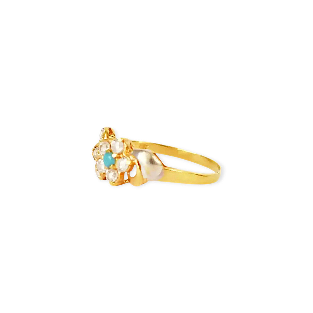 A close-up of a 21k gold ring with a flower-shaped setting, featuring a small round turquoise stone at the center surrounded by clear, brilliant zirconia stones, on a white background.