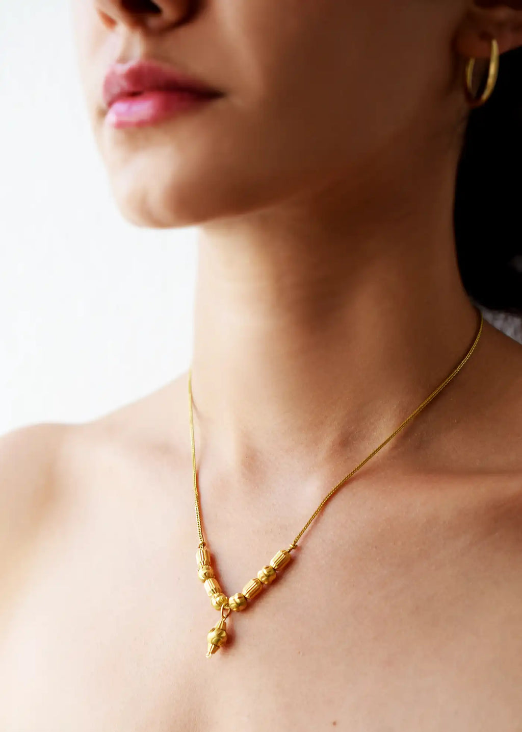 Elegant 21 Karat Yellow Gold Fox Tail necklace featuring a V-shaped arrangement of intricately textured gold beads and a matching central drop pendant, worn on a model's neck.