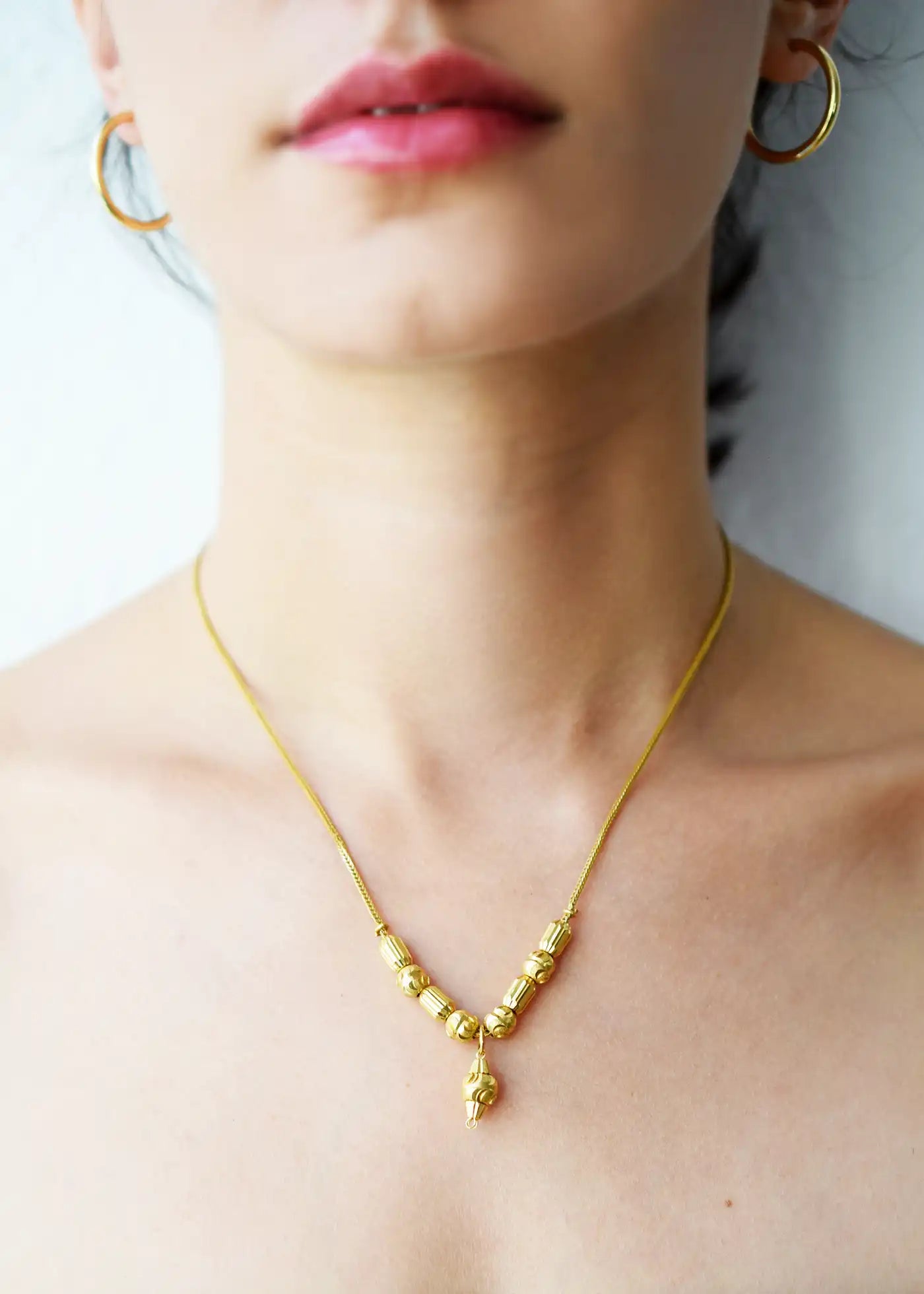 Elegant 21 Karat Yellow Gold Fox Tail necklace featuring a V-shaped arrangement of intricately textured gold beads and a matching central drop pendant, worn on a model's neck.