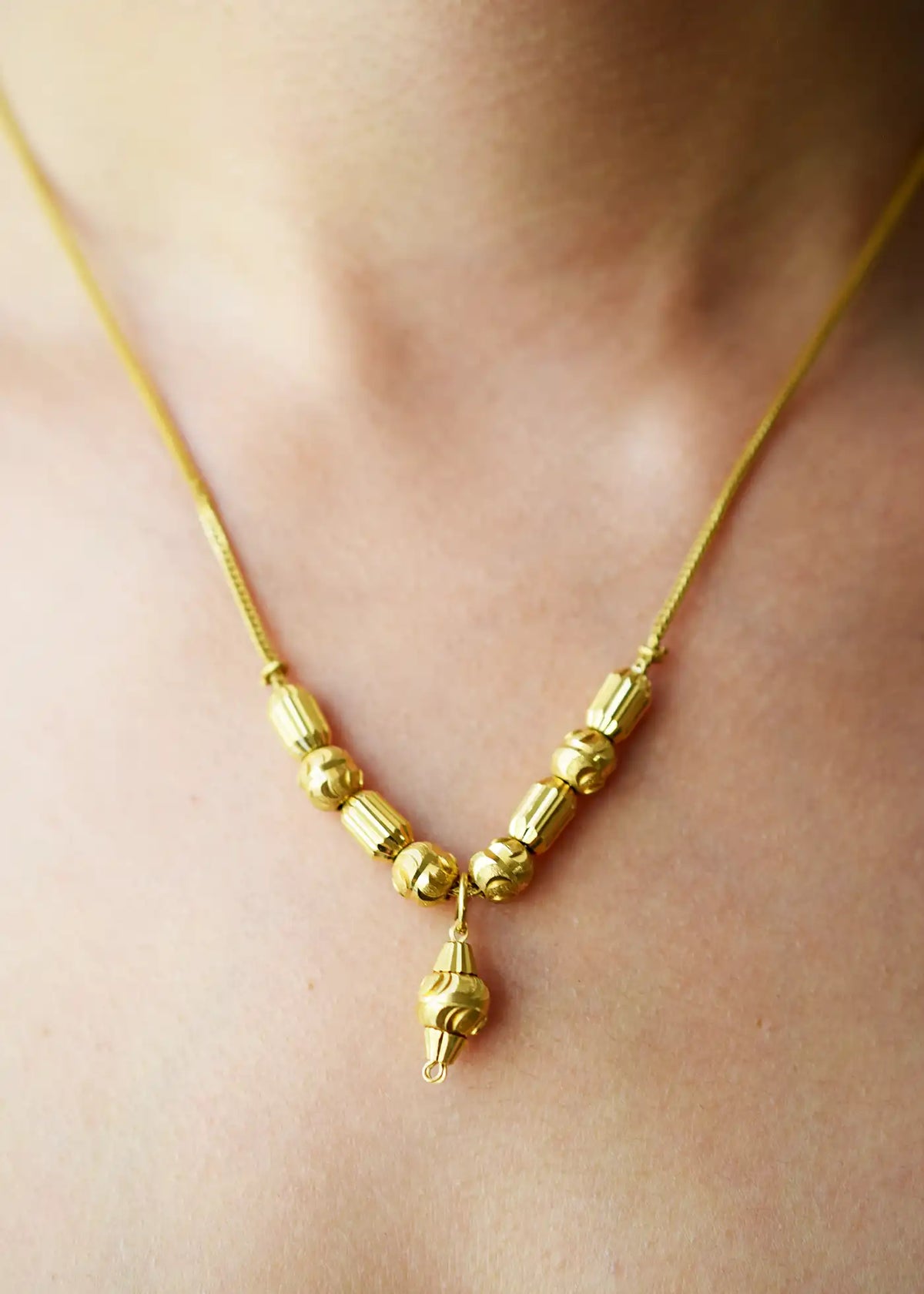 Elegant 21 Karat Yellow Gold Fox Tail necklace featuring a V-shaped arrangement of intricately textured gold beads and a matching central drop pendant, worn on a model's neck.