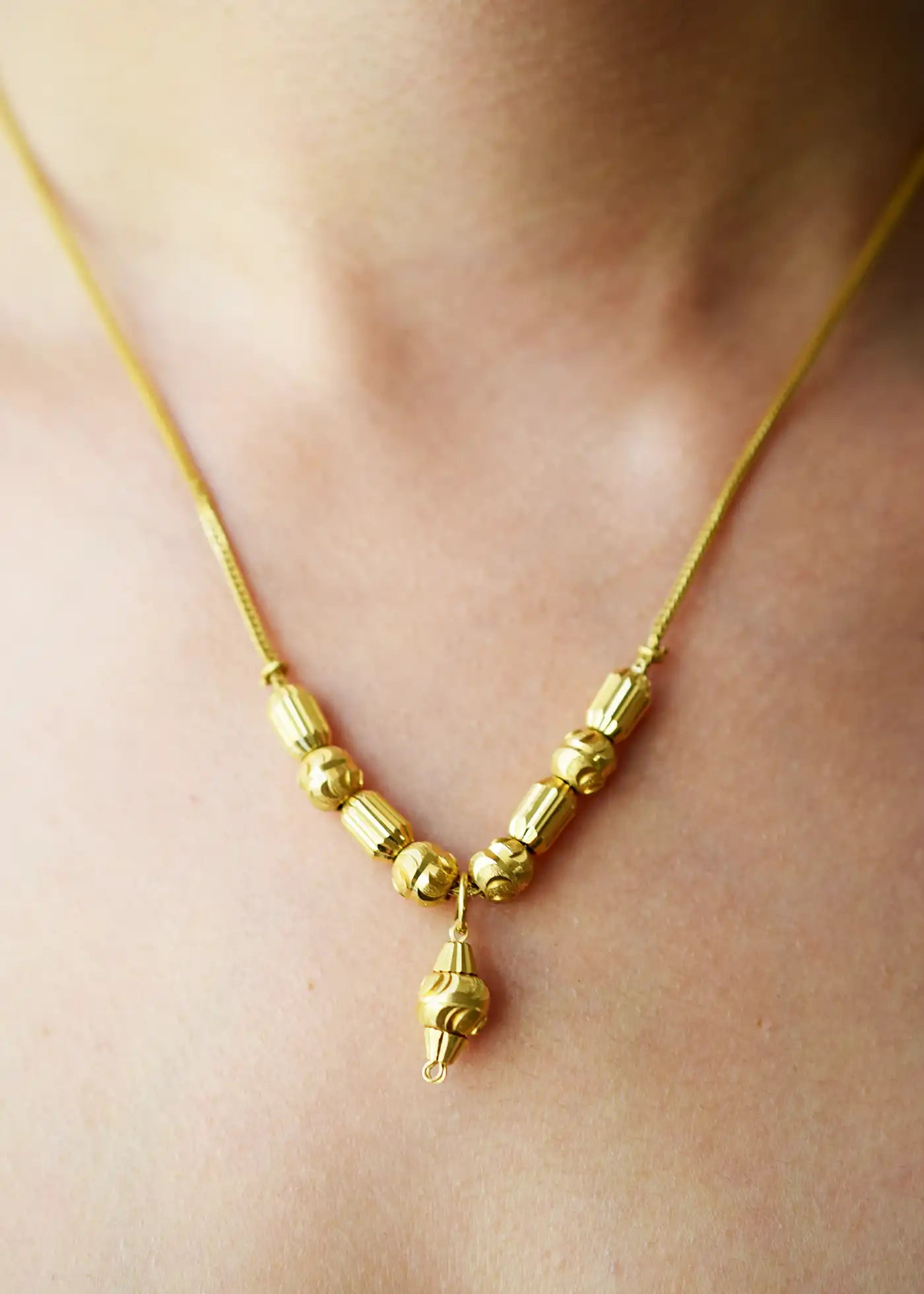 Elegant 21 Karat Yellow Gold Fox Tail necklace featuring a V-shaped arrangement of intricately textured gold beads and a matching central drop pendant, worn on a model's neck.