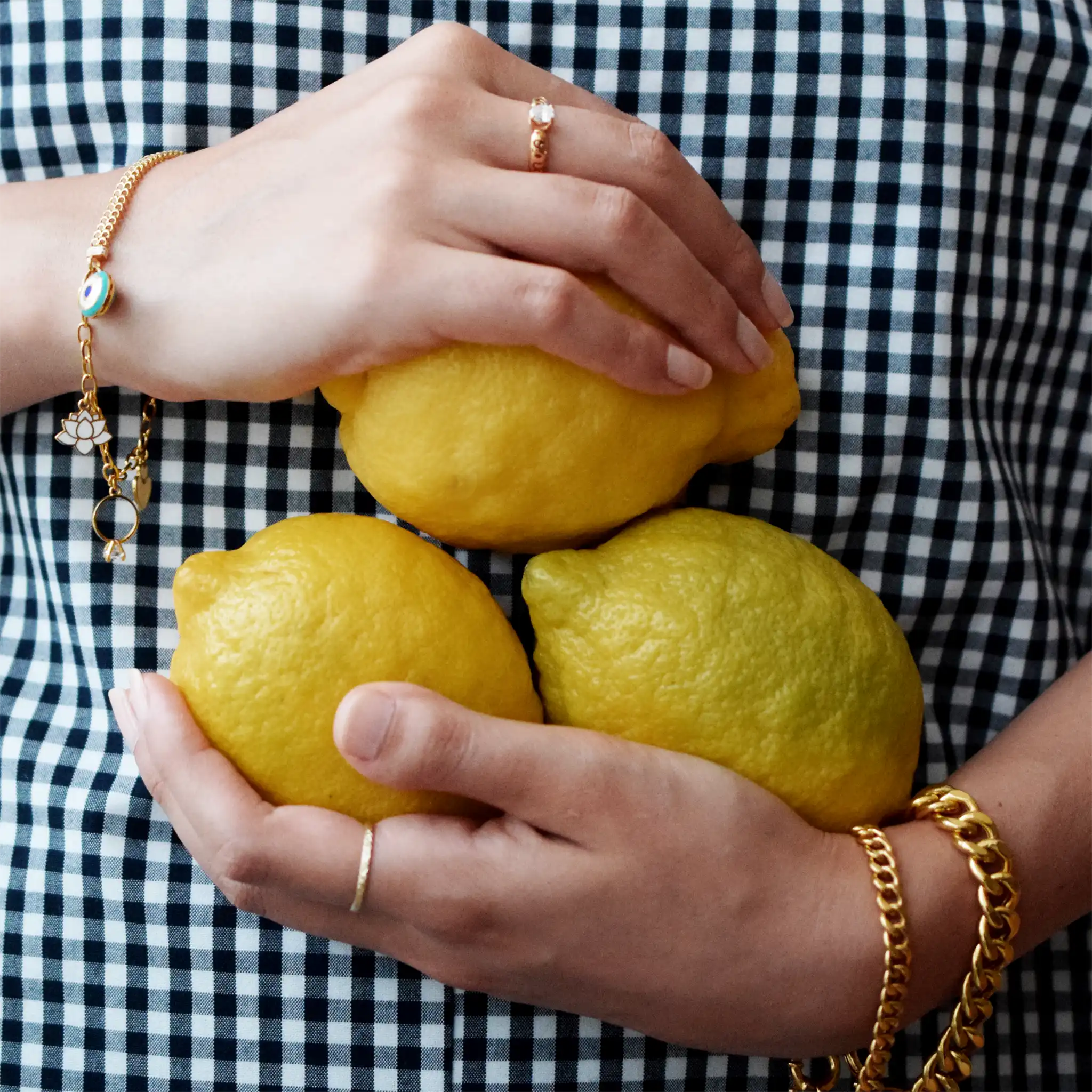 Elegant 21 Karat Yellow Gold double-chain charm bracelet, adorned with four diverse symbolic charms including a white lotus flower, a blue evil eye, and a miniature solitaire ring.