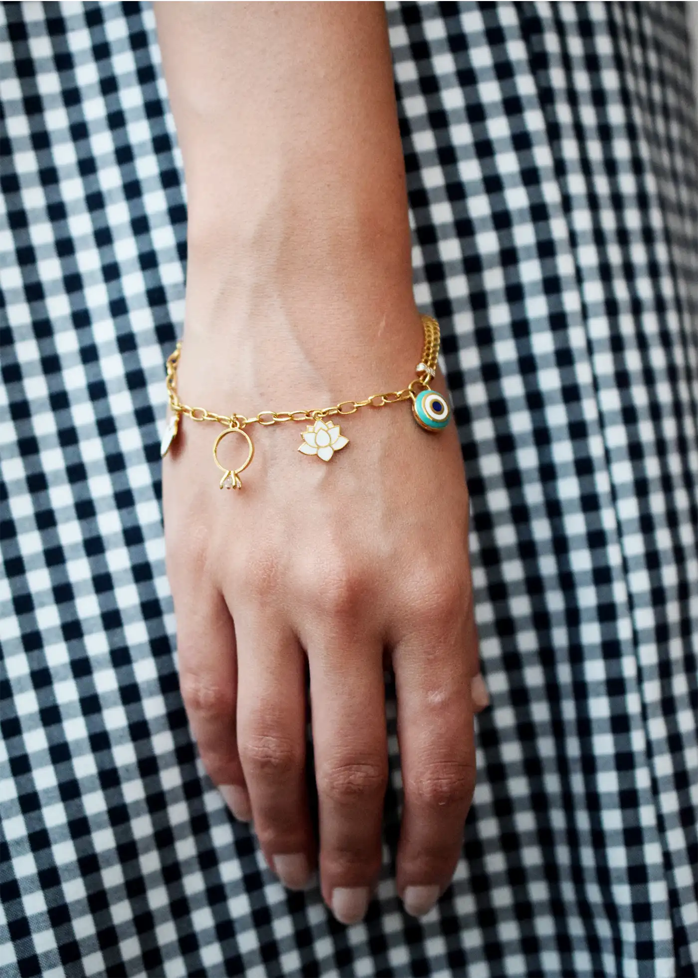 Elegant 21 Karat Yellow Gold double-chain charm bracelet, adorned with four diverse symbolic charms including a white lotus flower, a blue evil eye, and a miniature solitaire ring.