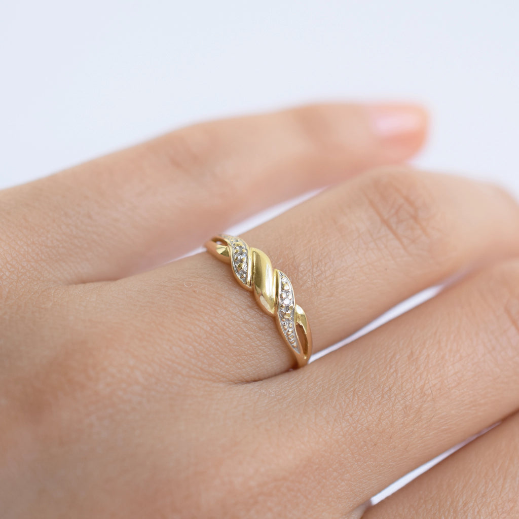 Gold ring with diamonds on a finger against a white background