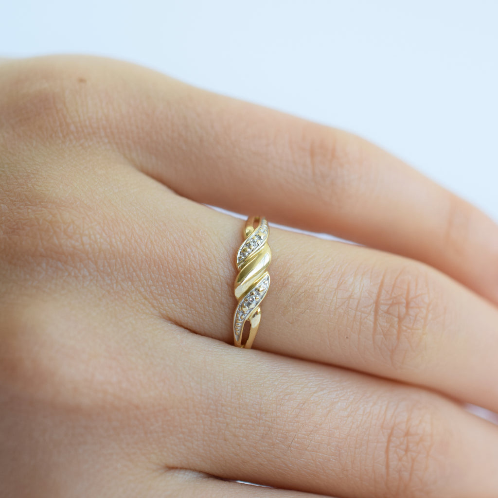 Gold ring with diamonds on a finger against a light background