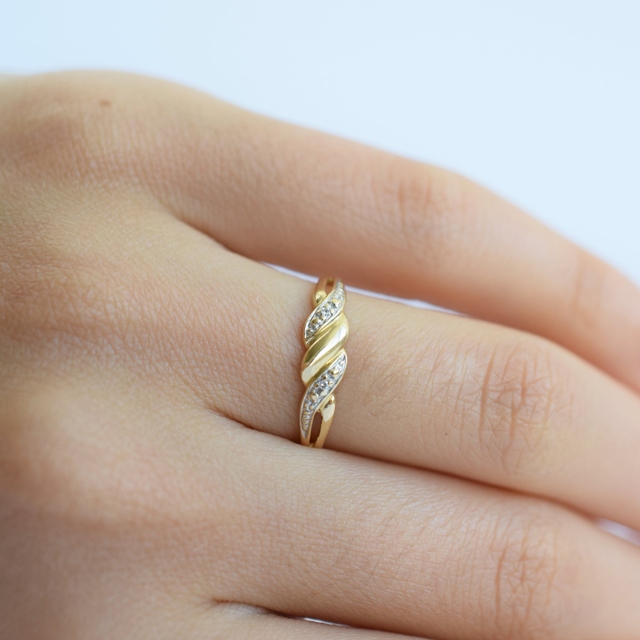Gold ring with diamonds on a finger against a light background