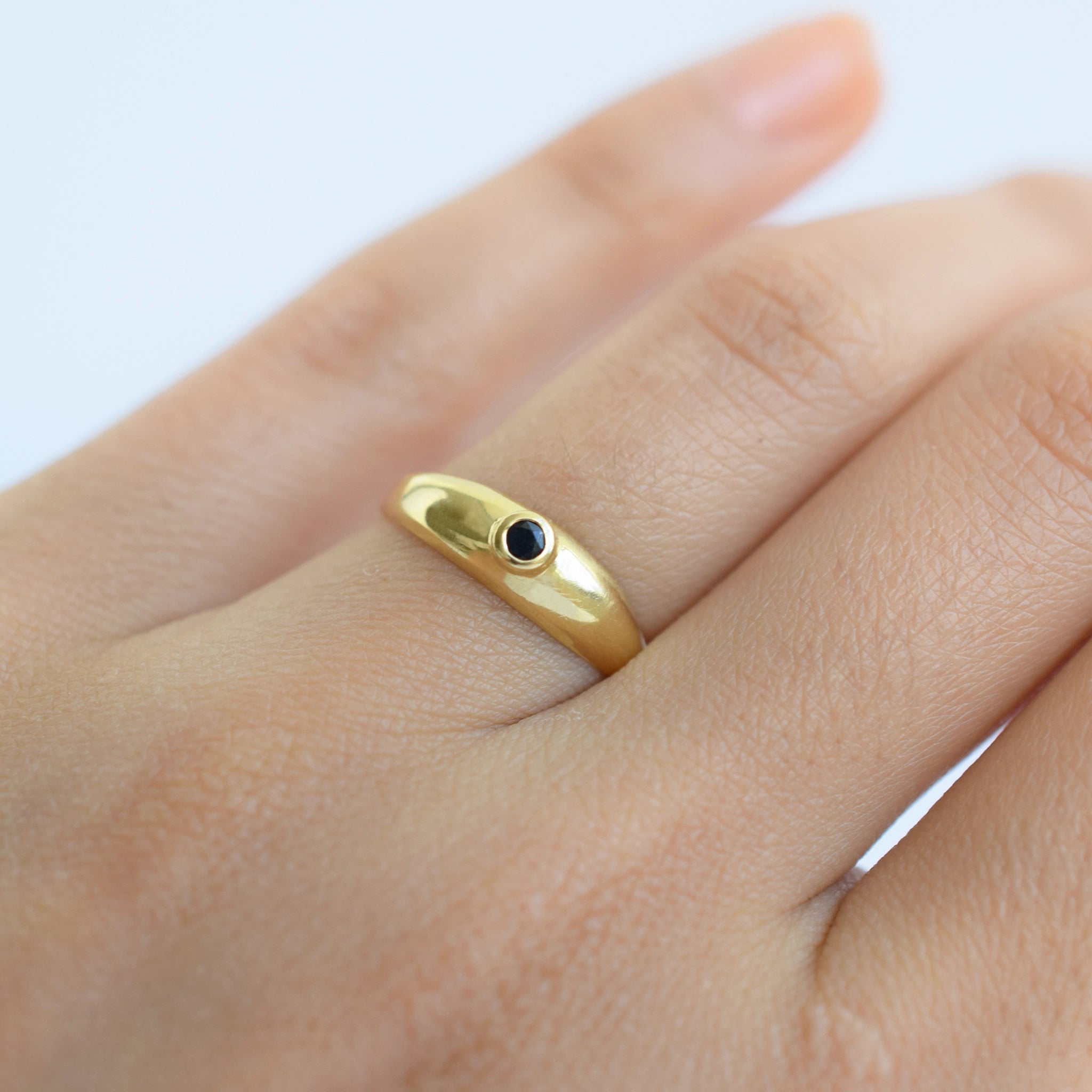 18 Karat Gold ring with a sapphire gemstone on a finger against a light background.