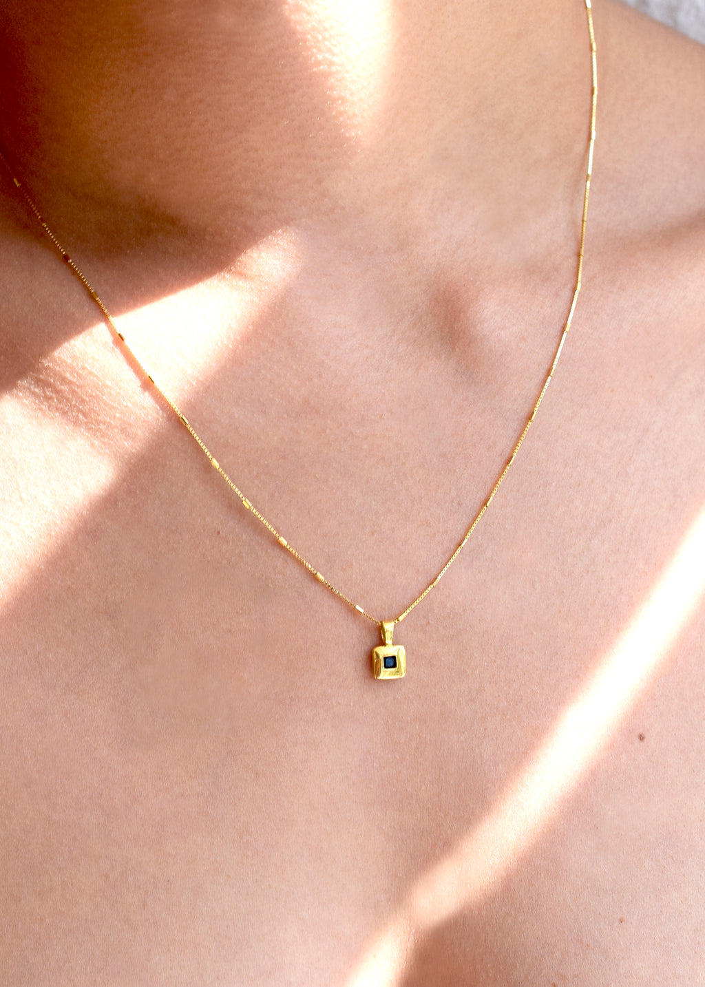Elegant 18 Karat Yellow Gold vintage pendant featuring a polished, diamond-shaped design with a central bezel-set square sapphire, worn on a models neck.