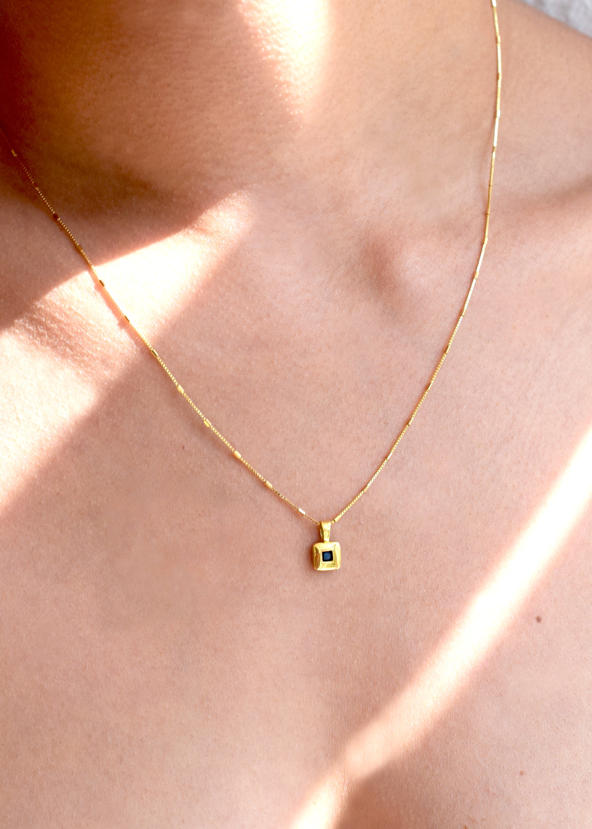 Elegant 18 Karat Yellow Gold vintage pendant featuring a polished, diamond-shaped design with a central bezel-set square sapphire, worn on a models neck.