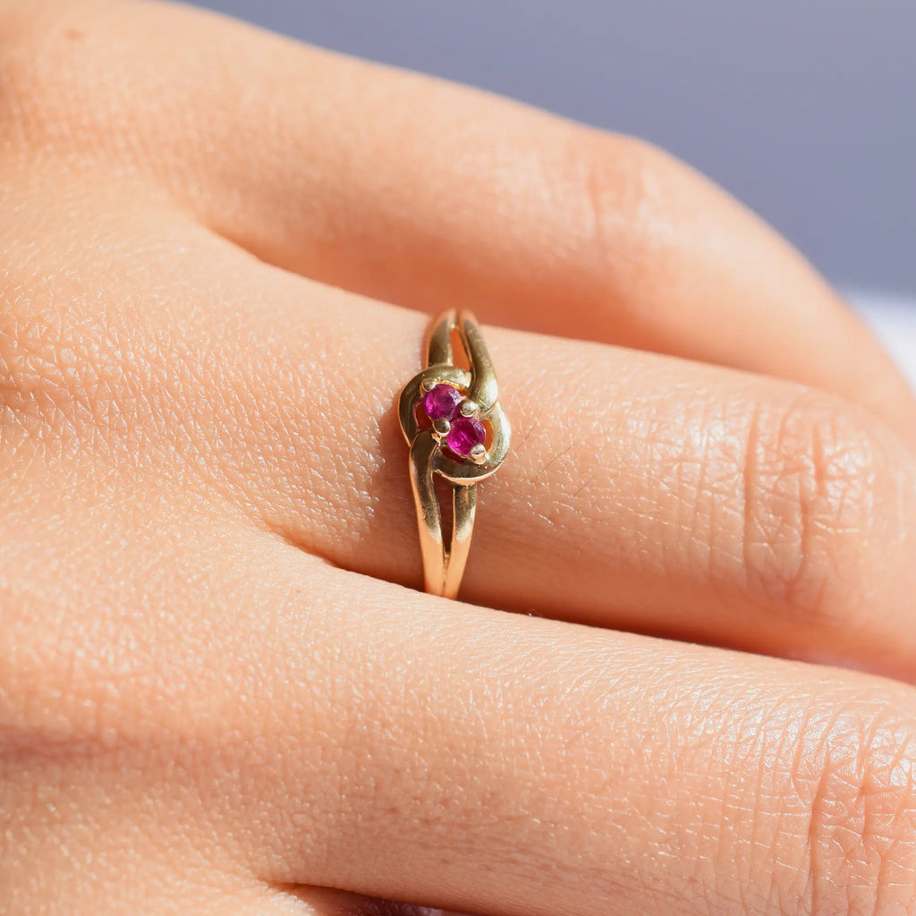 Elegant 18 Karat Yellow Gold vintage ring featuring two vibrant natural rubies nestled in a polished, swirling bypass setting, worn on a models hand.