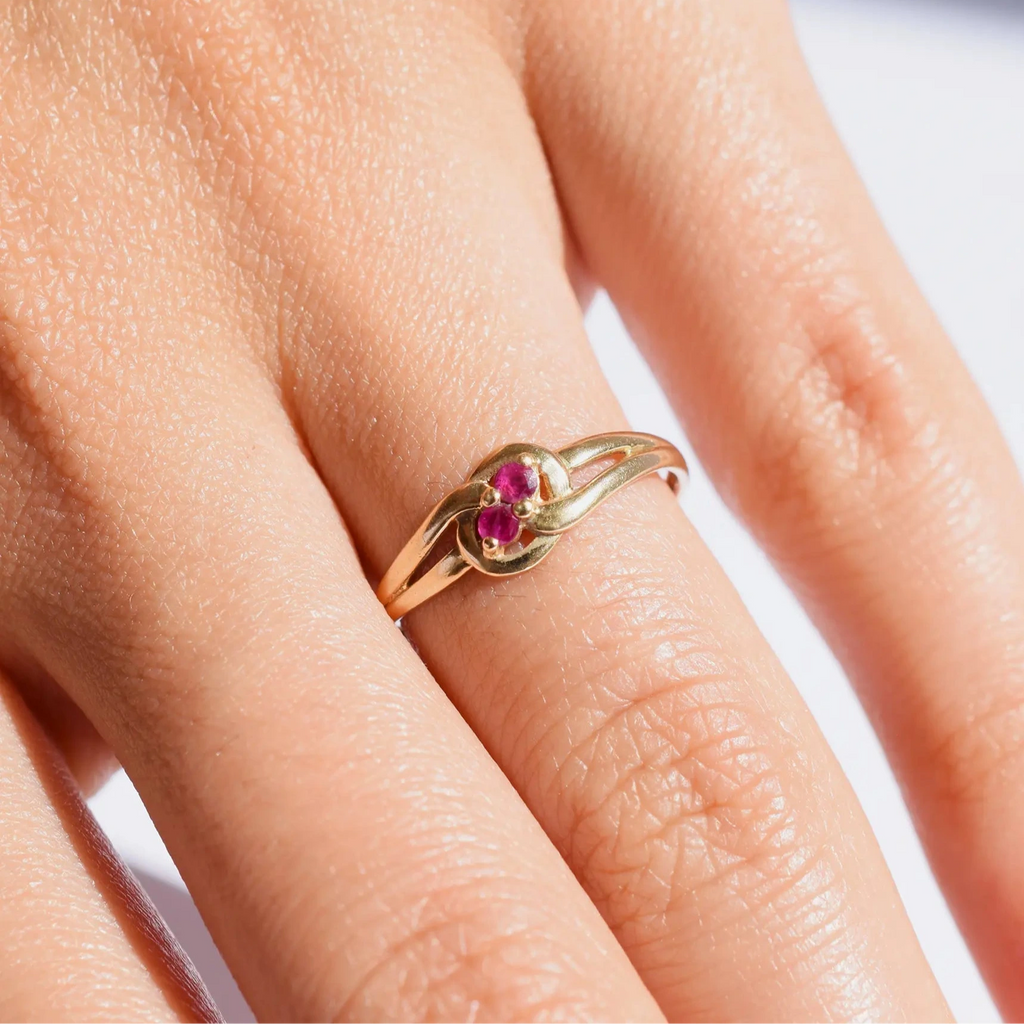 Elegant 18 Karat Yellow Gold vintage ring featuring two vibrant natural rubies nestled in a polished, swirling bypass setting, worn on a models hand.