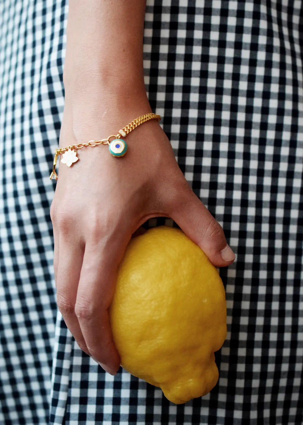 Elegant 21 Karat Yellow Gold double-chain charm bracelet, adorned with four diverse symbolic charms including a white lotus flower, a blue evil eye, and a miniature solitaire ring.