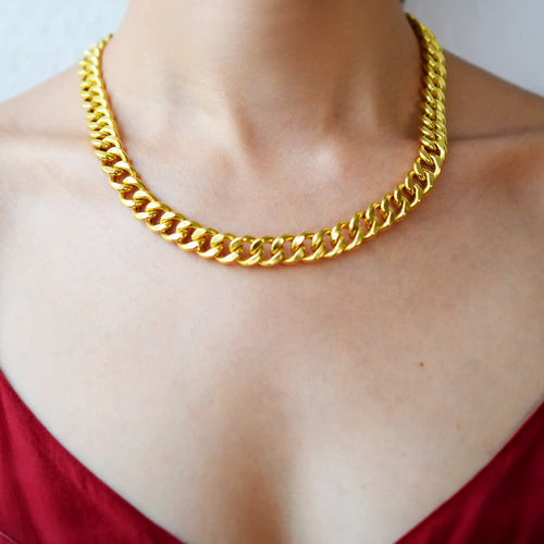 Luxurious 21 Karat Yellow Gold bold flat curb chain necklace, featuring an ornate clasp with black-enameled ornamental elements in a classic Greek key pattern, worn on a model's neck