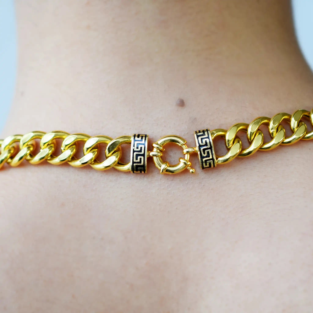 Luxurious 21 Karat Yellow Gold bold flat curb chain necklace, featuring an ornate clasp with black-enameled ornamental elements in a classic Greek key pattern, worn on a model's neck