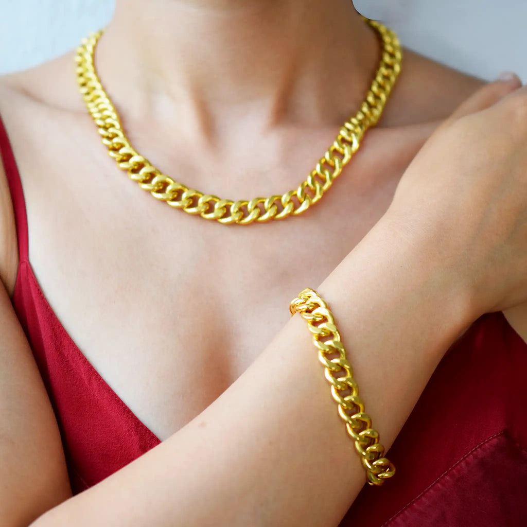 Luxurious 21 Karat Yellow Gold bold flat curb chain necklace, featuring an ornate clasp with black-enameled ornamental elements in a classic Greek key pattern, worn on a model's neck