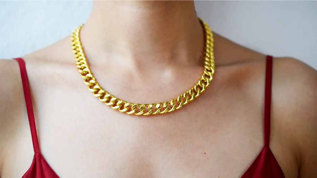Luxurious 21 Karat Yellow Gold bold flat curb chain necklace, featuring an ornate clasp with black-enameled ornamental elements in a classic Greek key pattern, worn on a model's neck