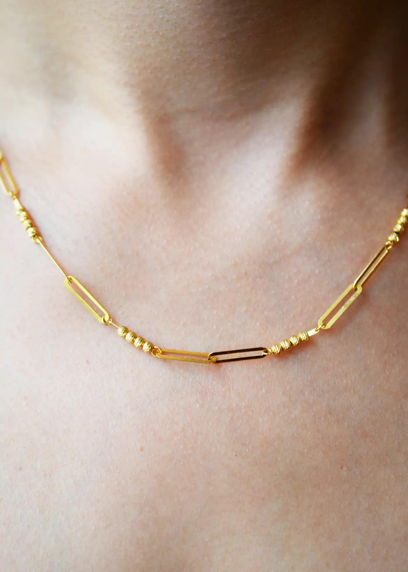 Modern 21 Karat Yellow Gold necklace featuring polished rectangular links alternating with clusters of sparkling diamond-cut beads, worn on a model's neck.