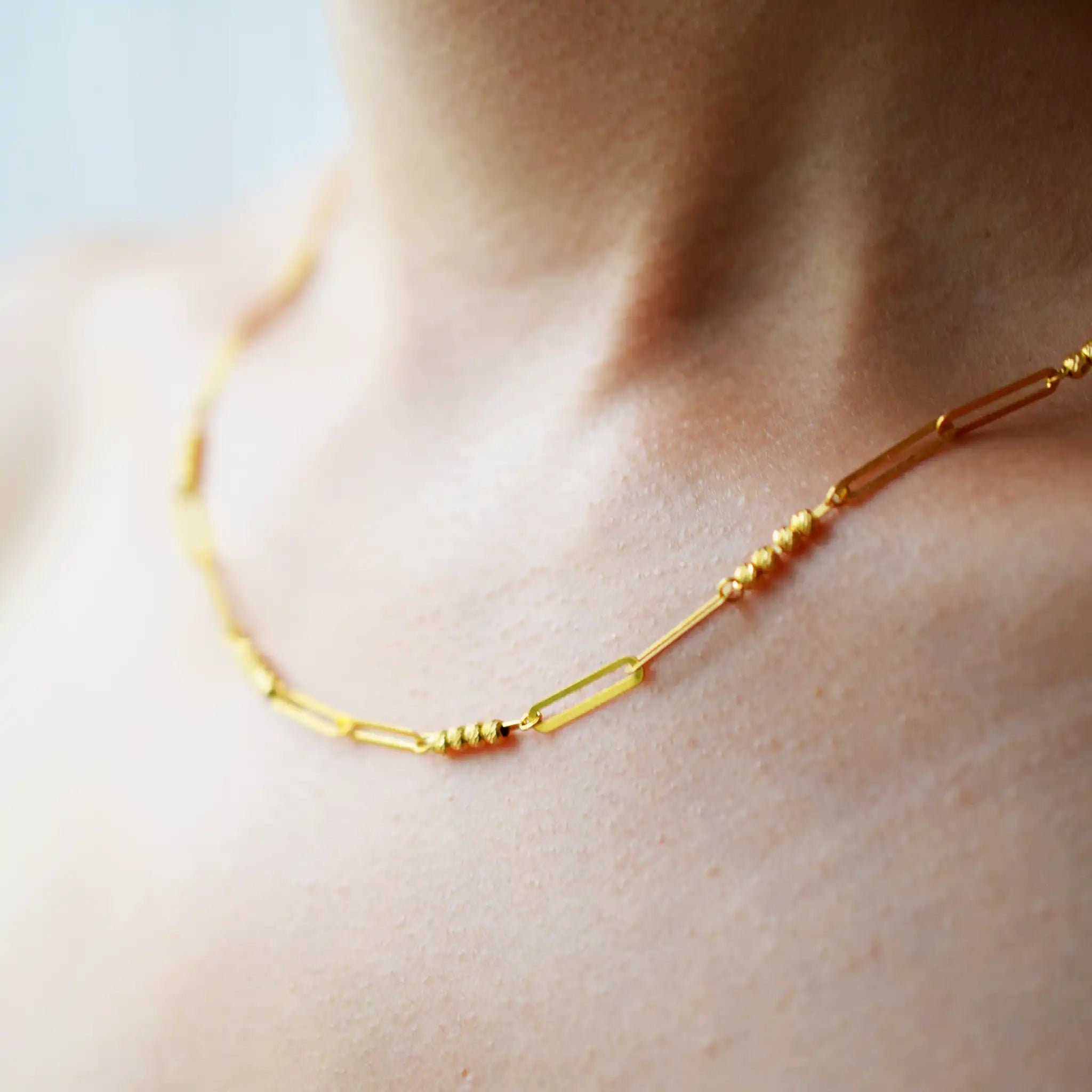 Modern 21 Karat Yellow Gold necklace featuring polished rectangular links alternating with clusters of sparkling diamond-cut beads, worn on a model's neck.