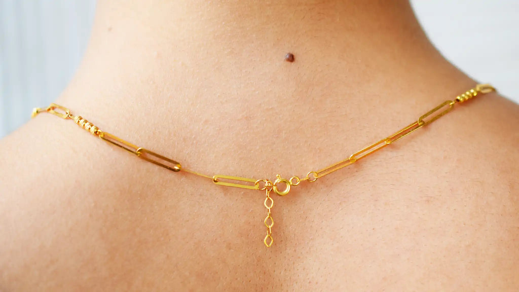 Modern 21 Karat Yellow Gold necklace featuring polished rectangular links alternating with clusters of sparkling diamond-cut beads, worn on a model's neck