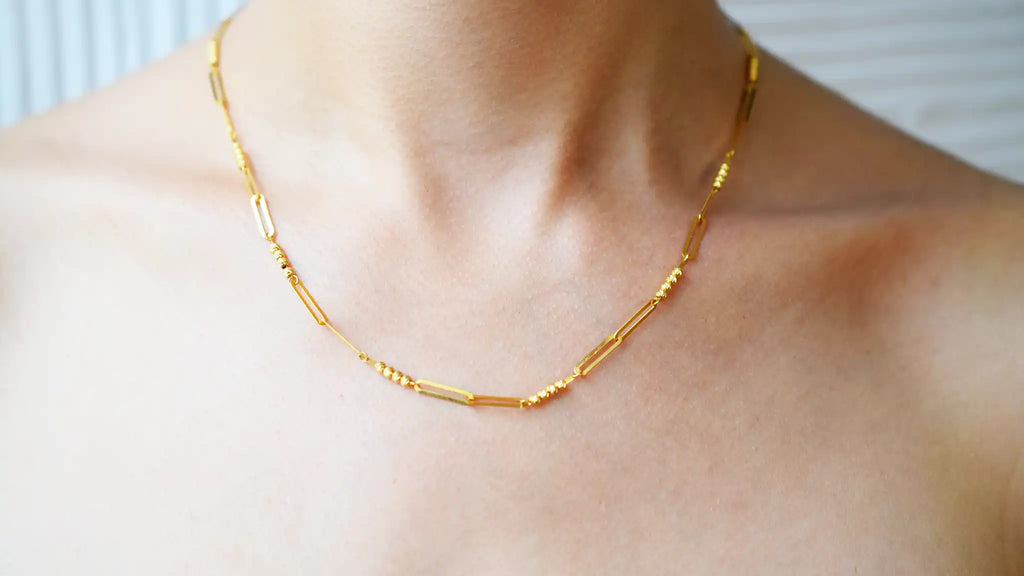 Modern 21 Karat Yellow Gold necklace featuring polished rectangular links alternating with clusters of sparkling diamond-cut beads, worn on a model's neck