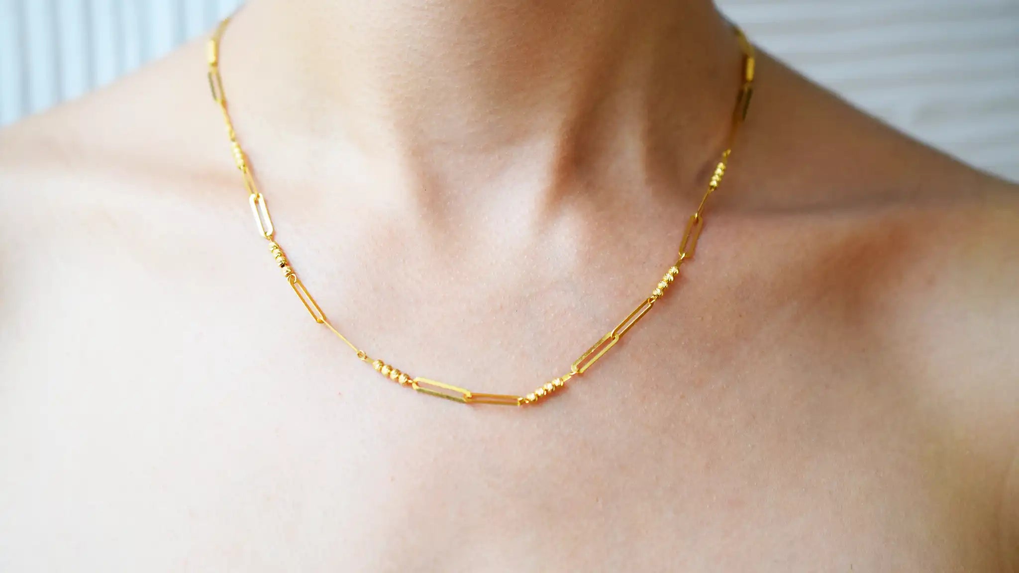 Modern 21 Karat Yellow Gold necklace featuring polished rectangular links alternating with clusters of sparkling diamond-cut beads, worn on a model's neck