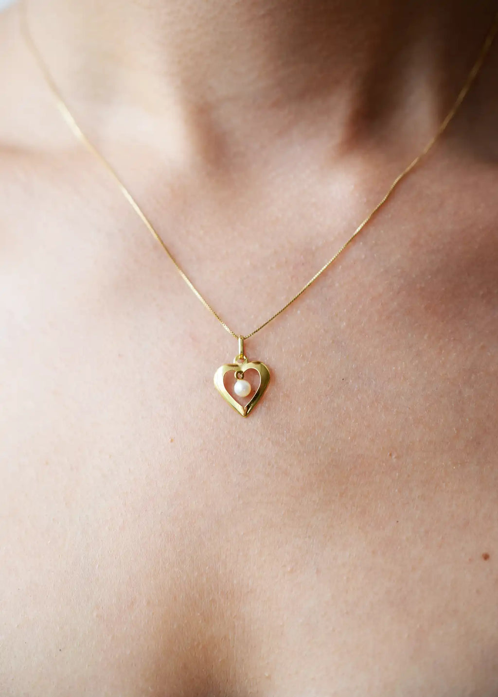 Romantic 18 Karat Yellow Gold heart pendant featuring a suspended freshwater pearl, worn on a delicate gold chain.