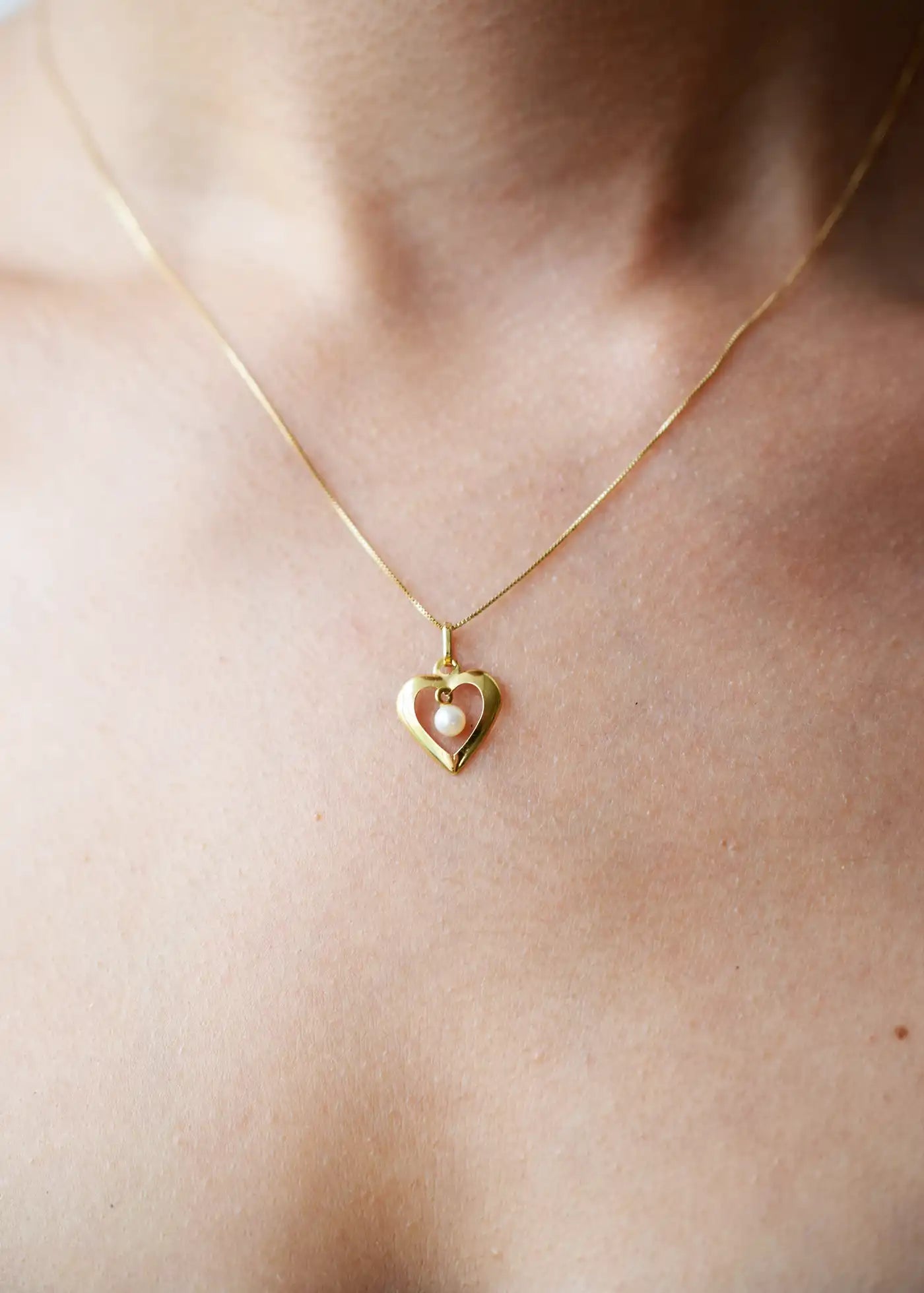 Romantic 18 Karat Yellow Gold heart pendant featuring a suspended freshwater pearl, worn on a delicate gold chain.