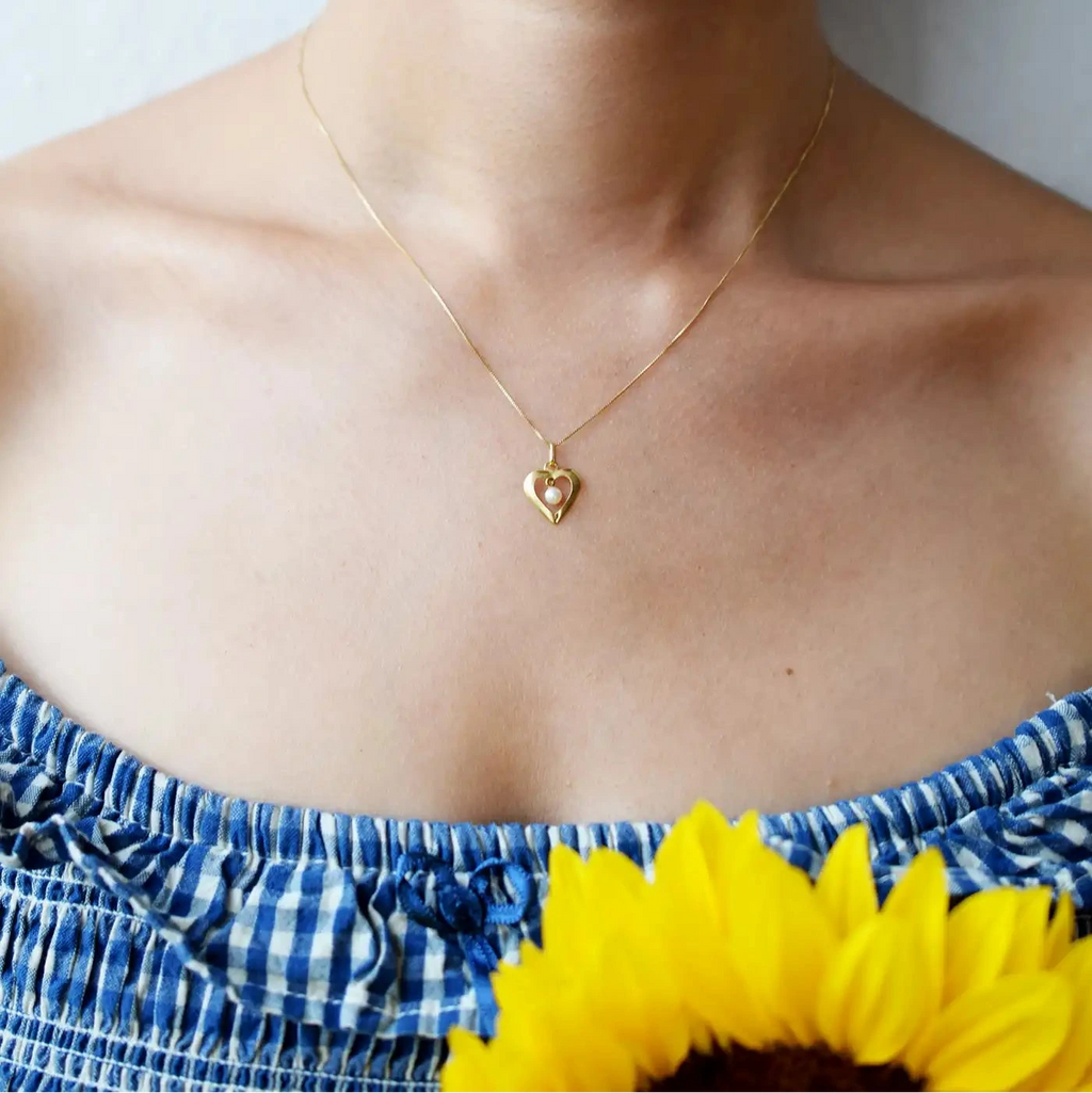 Romantic 18 Karat Yellow Gold heart pendant featuring a suspended freshwater pearl, worn on a delicate gold chain.