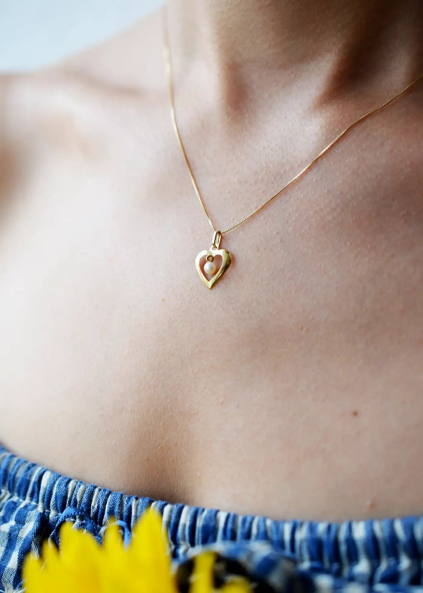 Romantic 18 Karat Yellow Gold heart pendant featuring a suspended freshwater pearl, worn on a delicate gold chain.