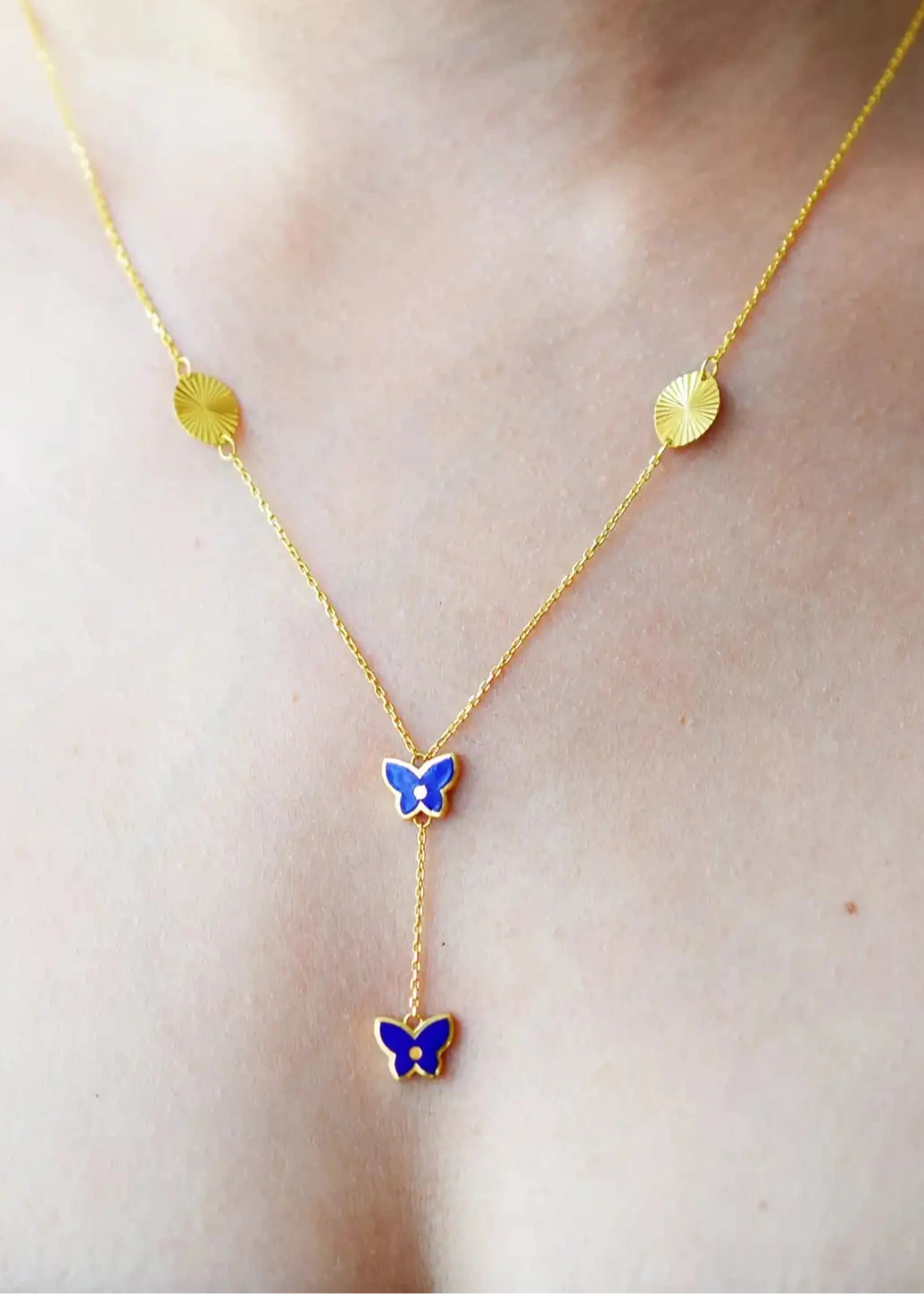 Vibrant 21 Karat Yellow Gold Y-necklace featuring two vivid blue enamel butterfly charms and two grooved gold disc stations along the chain, worn on a model's neck.