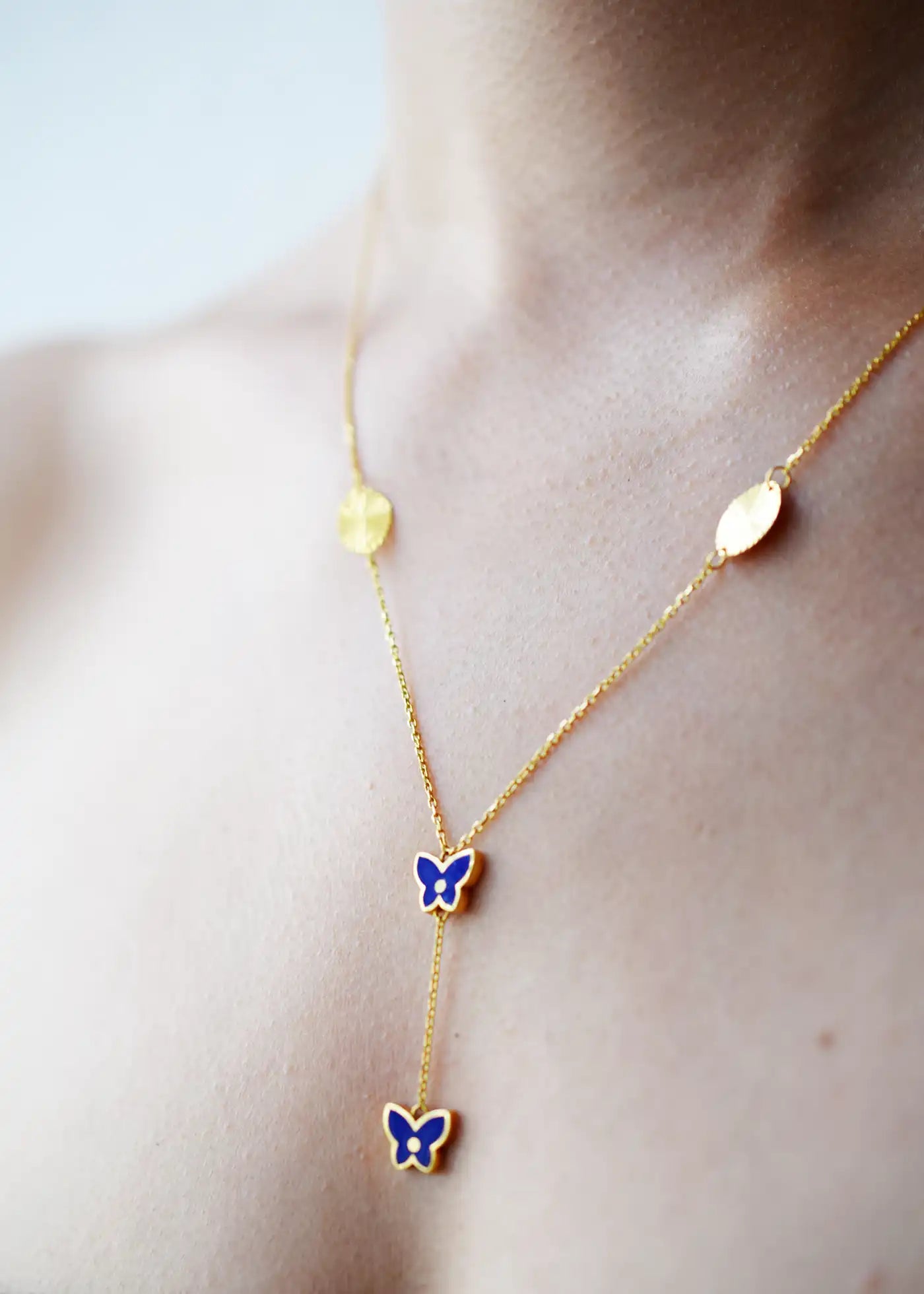 Vibrant 21 Karat Yellow Gold Y-necklace featuring two vivid blue enamel butterfly charms and two grooved gold disc stations along the chain, worn on a model's neck.